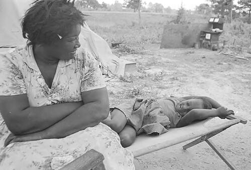 Figure 1. Woman and little girl on a cot in the dirt yard in front of the tent where they are living in Lowndes County, Alabama. Credit: Alabama Department of Archives and History.