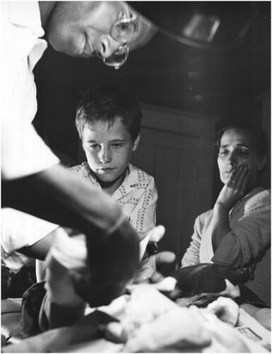 Figure 3 Unknown photographer, ‘A boy who cut his foot on a nail is treated by Dr Welch. After administering an injection of anti-tetanus serum, the physician sutured the wound and bandages it, as the mother looks on’. ‘A Doctor Makes His Rounds’, 1958. USIA ‘Picture Story’ Photographs, 1955–84, Record Group 306. 306-ST-460-58-24398.