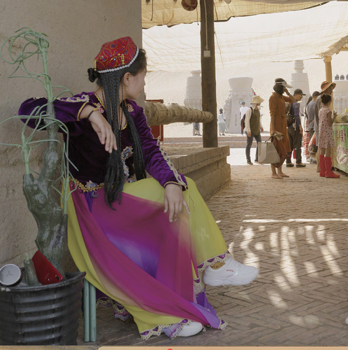 Figure 2. A Uyghur dancer rests in the shade while tourists purchase souvenirs near Turpan (Wack Citation2021).