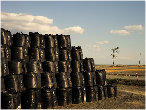 FIGURE 5 Rebecca Bathory, Untitled, 2016, photograph, from the Return to Fukushima series. It is a common decontamination practice to scrape the contaminated topsoil into black plastic “flexible containment bags” (furekon-bukuro), which are stacked at temporary storage site like those pictured above. By 2015, more than 9 million bags had accumulated across 100,000 sites in Fukushima (Mainichi Shimbun Citation2015). The need to find permanent disposal sites is among the many issues my research respondents hoped the Olympic Games would underscore. (For discussion, see Kirby Citation2021; Takahashi Citation2023a.)