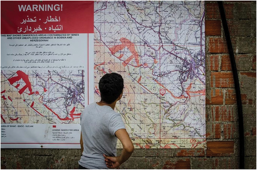 Figure 5. A young man in the Vučjak camp examines a map of the surrounding minefields (Photo: Thom Davies).