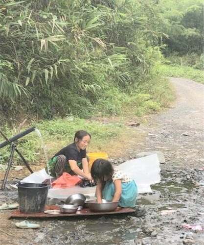 Figure 5. Mother and daughter washing clothes and kitchen utensils at the water pipes along the road site. Source: Author’s own photograph.